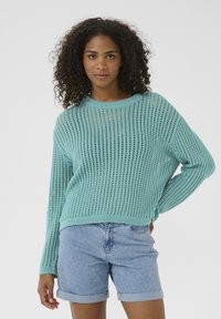 Maglione lavorato a maglia turchese chiaro con una vestibilità ampia, scollo tondo e un design a rete aperta, abbinato a pantaloni corti di denim arrotolati.