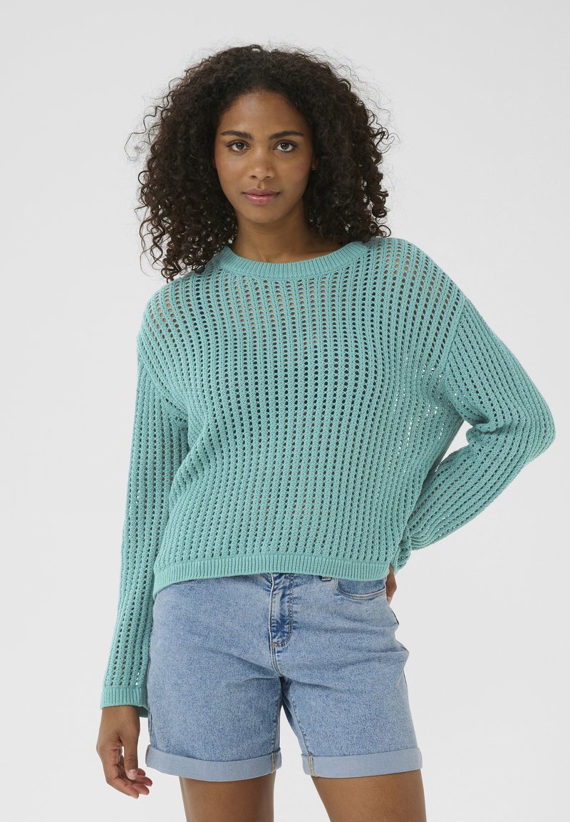 Maglione lavorato a maglia turchese chiaro con una vestibilità ampia, scollo tondo e un design a rete aperta, abbinato a pantaloni corti di denim arrotolati.