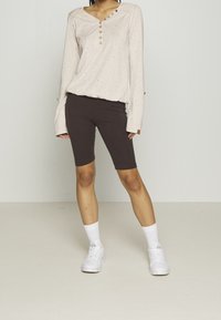 Light beige long-sleeve top with a textured pattern and button detail, paired with dark brown bike shorts. White sneakers and socks complete the outfit.