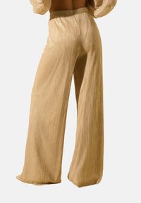 Pantalons dorés à jambes larges avec une texture côtelée et des accents brillants. Dotés d'une taille élastique pour un confort optimal et une liberté de mouvement fluide.
