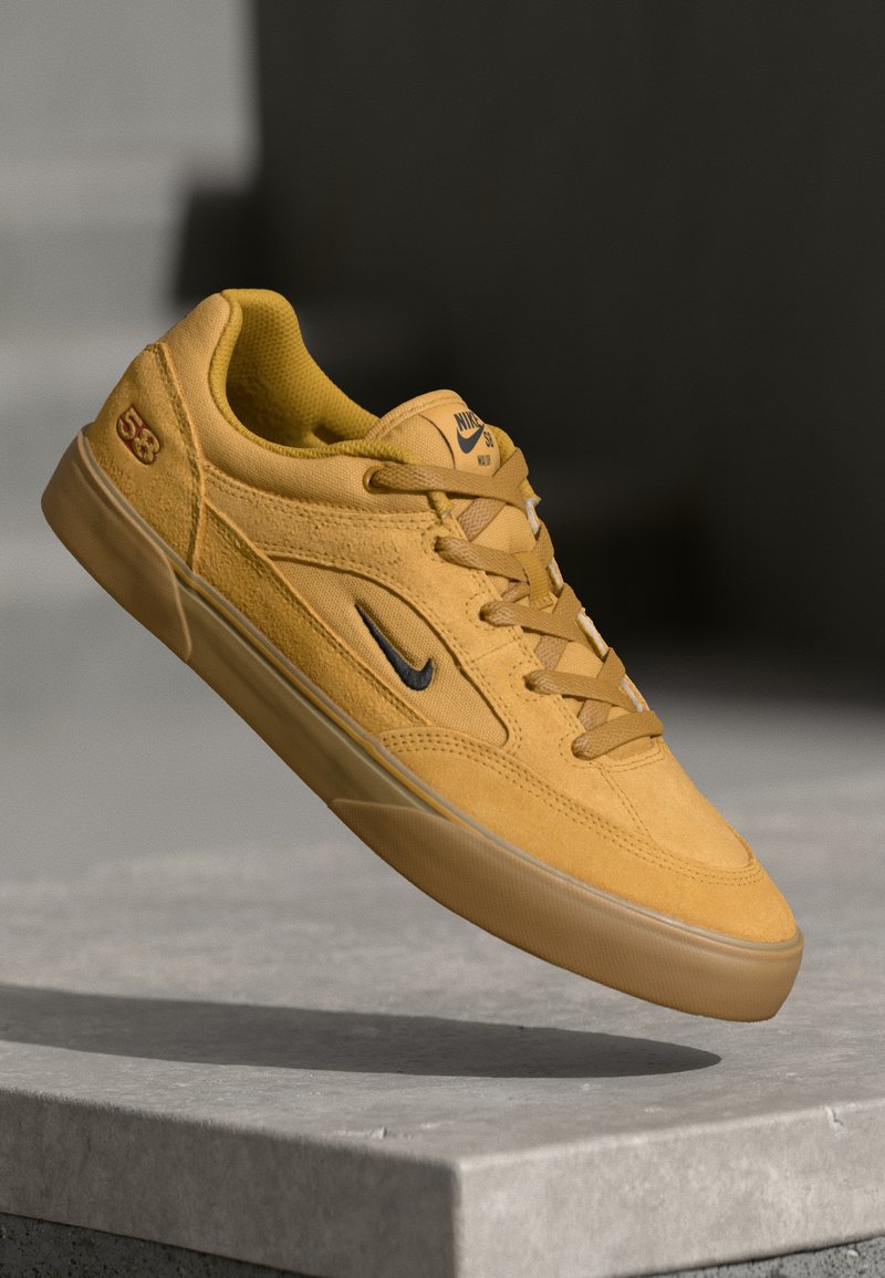 Żółte zamszowe sneakersy z gładką gumową podeszwą, z czarnym logo Nike, zaokrąglonym czubkiem oraz teksturowanymi akcentami po bokach i na języku.