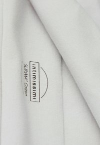 Tissu gris clair avec une texture lisse, présentant une étiquette sur laquelle est écrit "INTIMISSIMI SÜPIMA® Cotton." Design doux et simple.