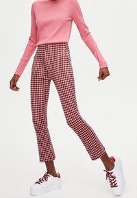 Czerwono-białe spodnie w kratę o dopasowanym kroju, zestawione z różowym, prążkowanym, długim rękawem oraz białymi sneakersami na platformie.