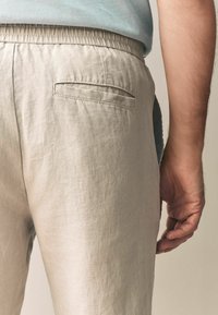 Lys beige linned bukser med elastisk talje, der har en baglomme med en vandret søm og en struktureret overflade.