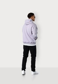 Light purple hoodie with a drawstring, worn over a white shirt, paired with black jeans and white sneakers. Simple, relaxed fit design.
