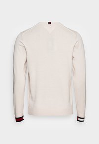 Cremfarbener Pullover mit langen Ärmeln, V-Ausschnitt und gerippten Bündchen, die am Saum mit einem dunklen roten, weißen und blauen Streifenakzent versehen sind.