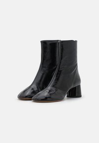 Černé kotníkové boty vyrobené z lesklé kůže, s špičatou špičkou, středním blokovým podpatkem a elegantním designem s hladkým povrchem.