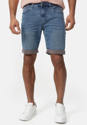 Denim shorts med en lys blå vask, slidte detaljer og opklippede kanter. Kombineret med hvide sneakers for et afslappet look.