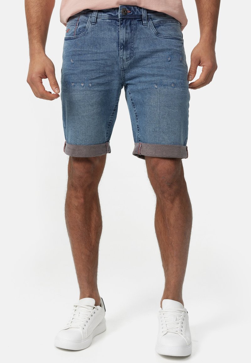 Shorts en denim avec un lavage bleu clair, des détails déchirés et un ourlet roulé. Associés à des baskets blanches pour un look décontracté.