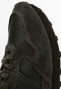 Tmavě šedá sportovní obuv z kombinace semiše a strukturované kůže, s výraznou gumovou podrážkou, kontrastním šitím a šněrováním.