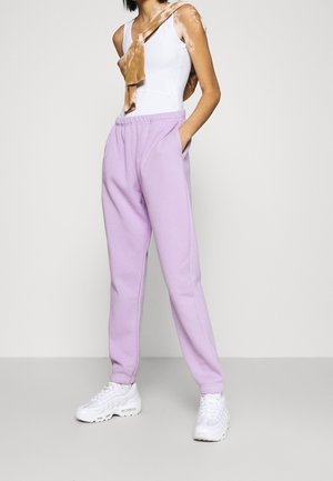 Lyse lilla sweatpants lavet af blødt stof, med elastisk talje og sidelommer, parret med hvide sneakers og et brunt tørklæde.