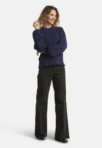 Maglione blu navy a treccia con maniche ampie, abbinato a pantaloni neri a zampa d'elefante. L'outfit presenta una vestibilità comoda e un tessuto testurizzato.