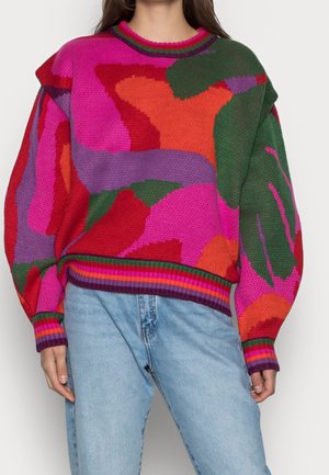 Suéter de punto de colores brillantes con patrones abstractos en rojo, rosa, verde, naranja y púrpura, combinado con pantalones vaqueros de mezclilla azul claro.