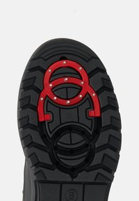 Sort ydersål med dybe slidmønstre; har tre røde cirkulære accenter og sølvfarvede nitter for ekstra greb. Robust gummimateriale.