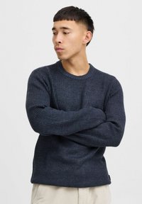 Navy blue ribbed knit sweater with a round neckline and long sleeves, featuring a textured fabric and a relaxed fit. Subtle logo detail at hem.