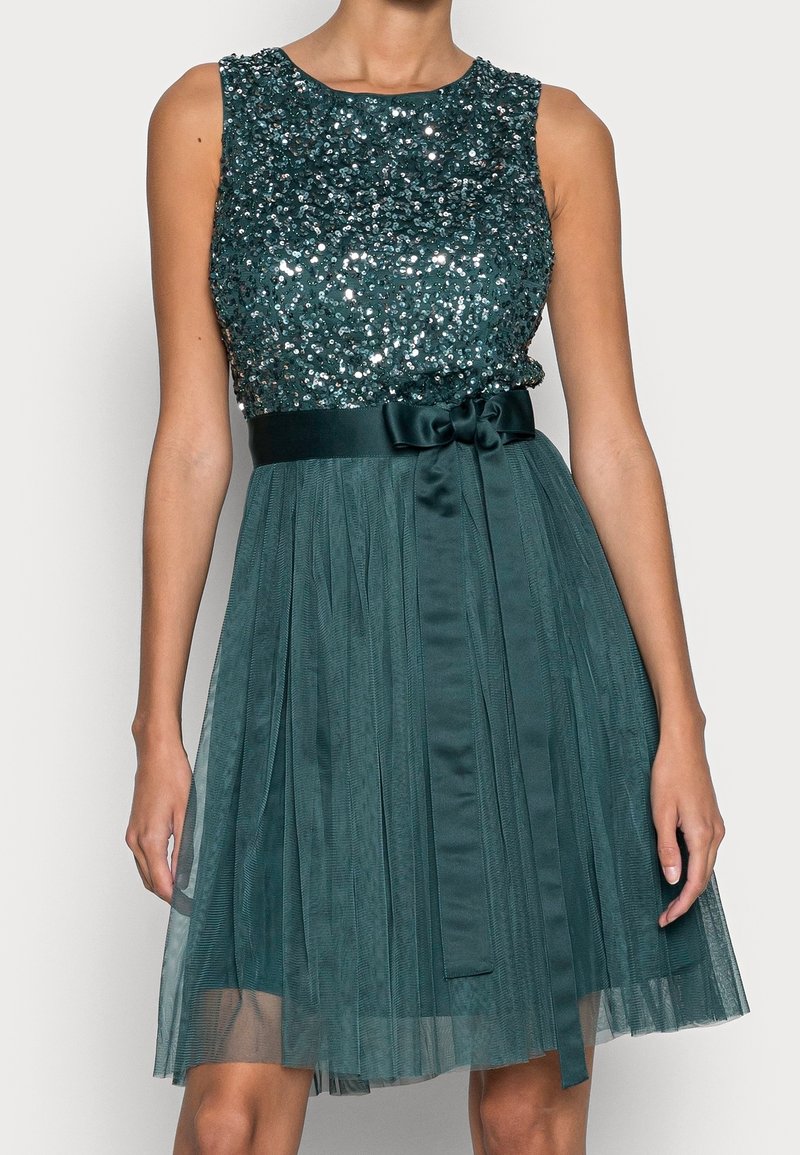 Robe verte sans manches avec corsage en sequins, ceinture en satin nouée en nœud et jupe en tulle plissé.