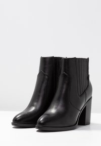 Bottes noires à la cheville en cuir lisse, avec panneaux latéraux côtelés, bout pointu et talon bloc. Design simple et élégant.