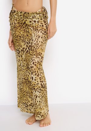 Woman wearing a long, leopard-print wrap skirt tied at the hips, standing barefoot against a plain white background.