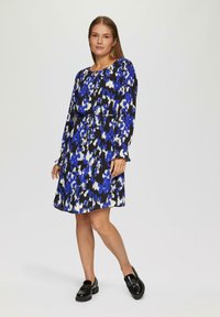 Langemouwige jurk in een blauw-wit abstract patroon op een zwarte achtergrond. Kenmerkt zich door een getailleerde taille en een vloeiende rok; gemaakt van lichtgewicht stof.
