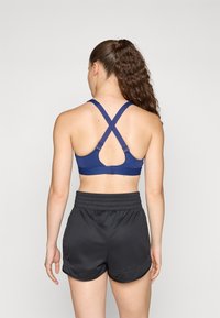 Mörkblå sportbh med korsade band och justerbara hakar, som matchas med svarta träningsshorts med elastisk midja.