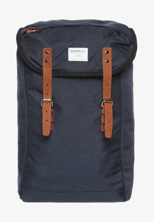 Dunkelblauer Stoff-Rucksack mit braunen Leder-Schnallenriemen und einem weißen Etikett mit der Aufschrift Sandqvist Urban Outdoor.