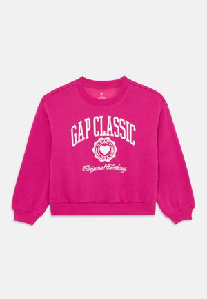 Fuksia genser laget av bomull, med rund hals og ribbestrikkede ermer. Frontgrafikken viser "GAP CLASSIC" i hvit tekst.