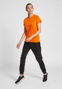 Orange kortärmad T-shirt ihop med svarta joggerbyxor och svarta sneakers, med en avslappnad passform och mjuk bomullstextur.