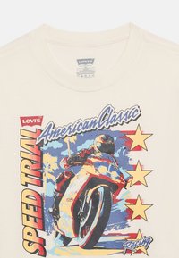 Αναβάτης μοτοσυκλέτας με πλήρη εξοπλισμό, γέρνοντας σε μια στροφή με φοίνικες, αστέρια και το κείμενο "SPEED TRIAL American Classic Racing" σε λευκό πουκάμισο.