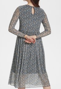 Vestido azul de manga larga con textura transparente, cintura fruncida y detalle de espalda con abertura en forma de llave, con pequeños motivos florales multicolores.