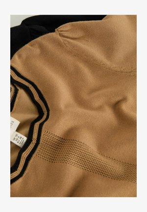 Bežová látka s texturovaným povrchem, s černým výstřihem a pruhem s síťovaným vzorem. Cedulka s pokyny k údržbě viditelná na levé straně.