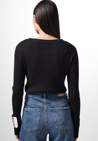 Maglione nero a coste con scollatura ampia, design aderente, maniche lunghe, abbinato a jeans in denim blu a vita alta con tasche posteriori.