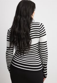 Schwarz-weiß gestreifter, gerippter Pullover mit langen Ärmeln und taillierter Passform, der wechselnde breite und schmale Streifen zeigt.