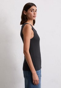 Zwart geribbeld tanktop met een aansluitend ontwerp, brede schouderbanden en een gladde textuur, gecombineerd met lichtblauwe denim jeans.