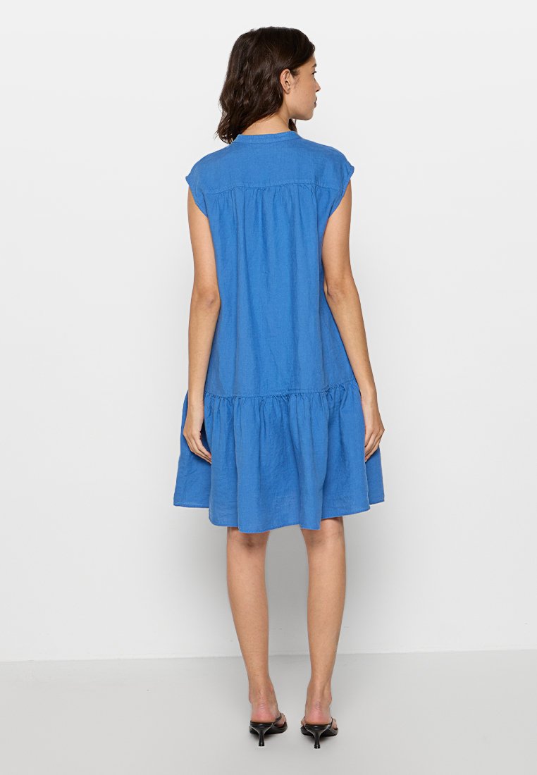 Niebieska lniana sukienka z krótkimi rękawami i falbanistą spódnicą. Posiada okrągły kołnierzyk oraz luźny krój, sięgający powyżej kolan.
