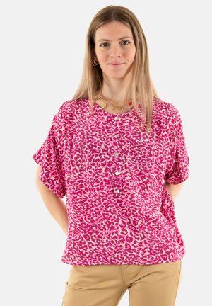 Blouse rose à manches courtes avec un motif imprimé léopard, présentant des détails de boutons sur le devant et une coupe décontractée. Le tissu a une texture douce.