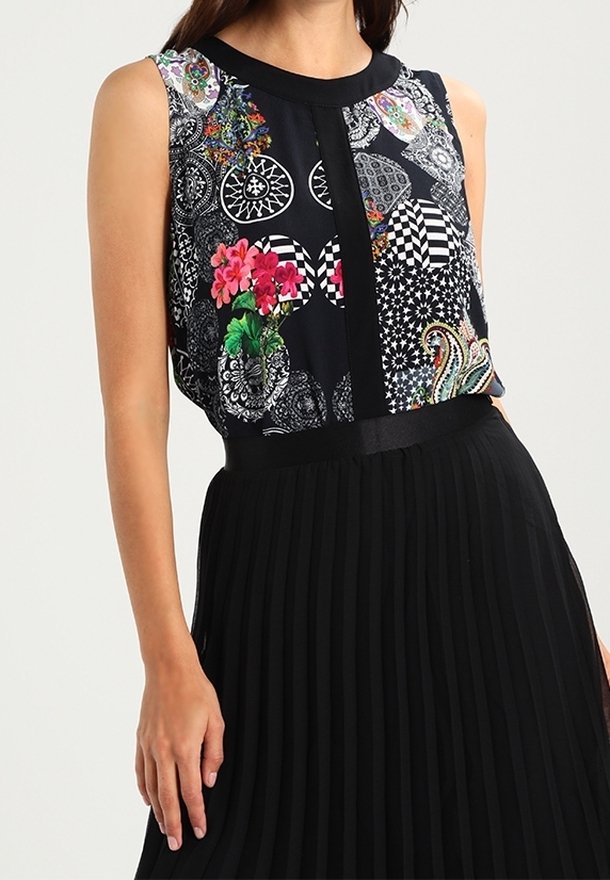 Femme portant un haut noir sans manches avec des motifs floraux et géométriques colorés, assorti à une jupe plissée noire taille haute.