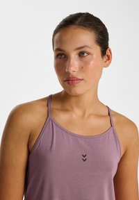 Débardeur de sport violet avec fines bretelles, encolure arrondie, et un motif chevron subtil en brun foncé sur le devant. Texture de tissu douce.