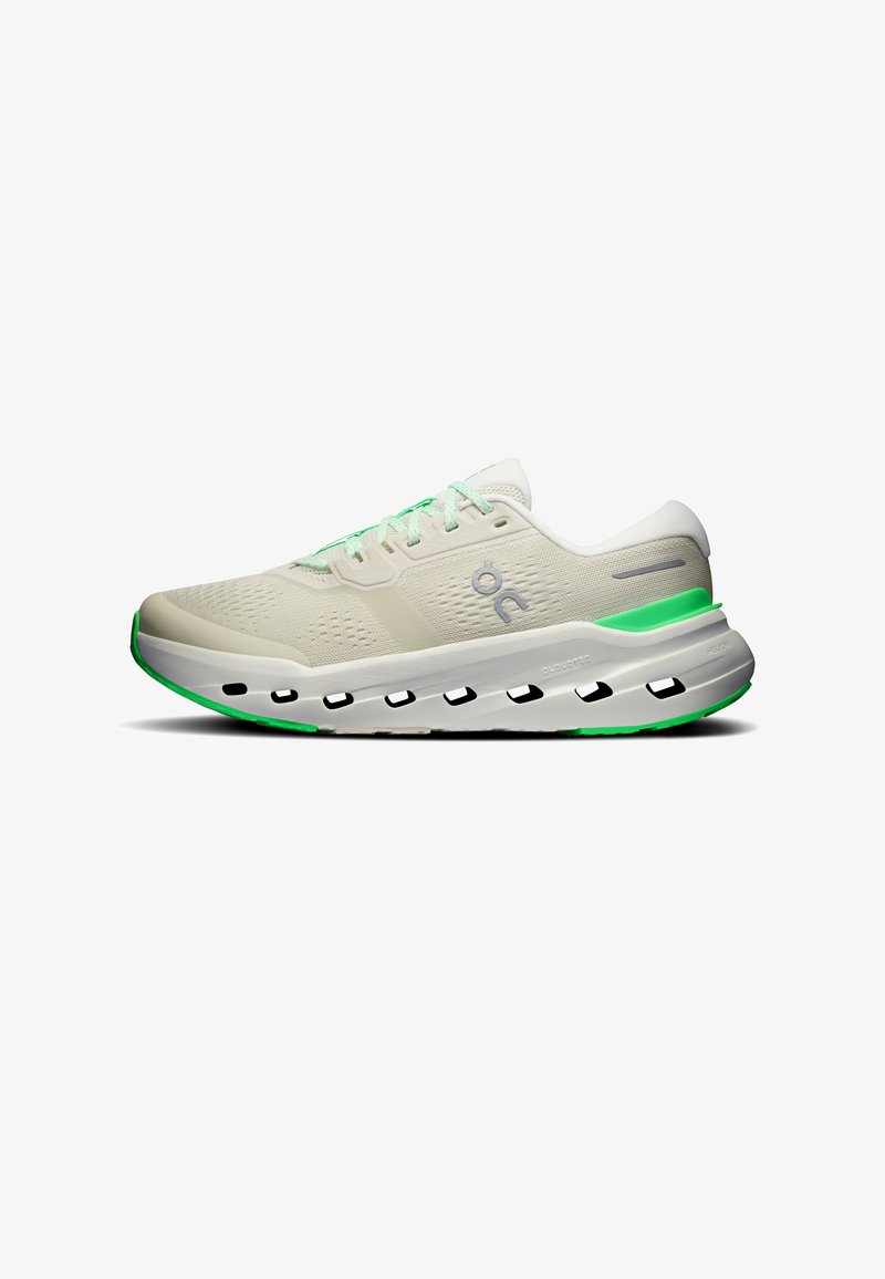 Chaussure de course beige avec des accents verts, semelle épaisse et rembourrée, trous de ventilation et logo latéral, présentée sur fond blanc.
