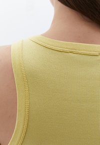 Ribbad gul linne med breda axelband, med en slät textur och sydd halsringning, sedd bakifrån.