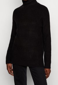 Maglione a collo alto nero a costine con una vestibilità comoda, dotato di maniche lunghe e una texture lavorata a maglia. Abbinato a pantaloni scuri.
