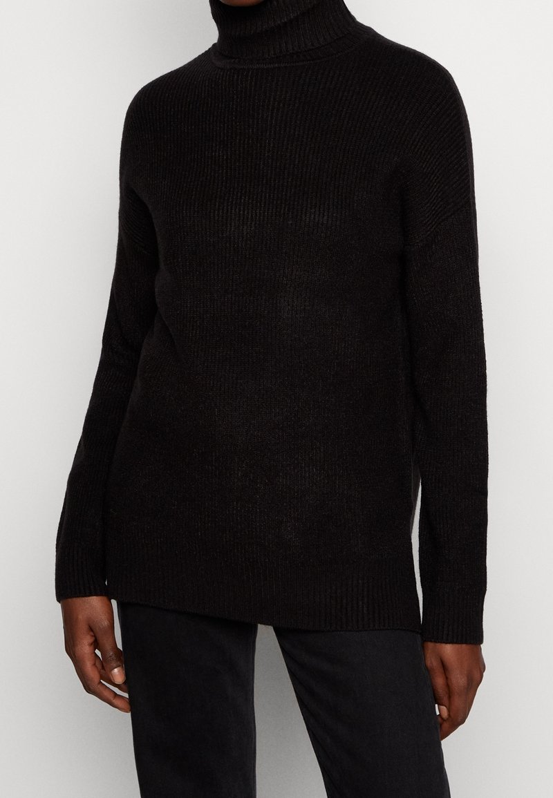 Maglione a collo alto nero a costine con una vestibilità comoda, dotato di maniche lunghe e una texture lavorata a maglia. Abbinato a pantaloni scuri.