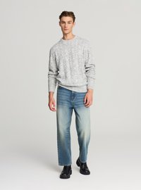 Jasnoszary sweter z dzianiny w splot warkoczowy, z okrągłym dekoltem, zestawiony z wyblakłymi niebieskimi dżinsami o prostych nogawkach oraz czarnymi masywnymi butami.
