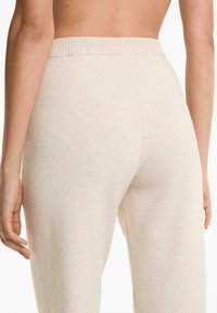 Close-up of a person’s lower back and hips wearing light beige knit pants with an elastic waistband.