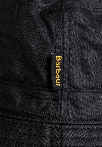 Chapeau noir fait de tissu durable avec un design surpiqué, comportant une étiquette "Barbour" jaune bien en vue sur le côté.