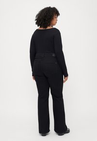 Black ribbed long-sleeve top paired with black flared jeans, featuring a straight waistband and back pockets. Smooth texture, casual design.