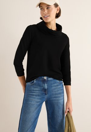 Top nero con collo a caramella e maniche a tre quarti, abbinato a jeans dritti blu chiaro. I jeans presentano un motivo testurizzato e strisce laterali.
