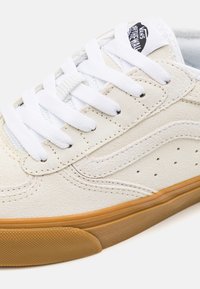 White suede sneaker with a textured finish, contrasting gum rubber sole, white laces, and subtle perforations on the side for ventilation.