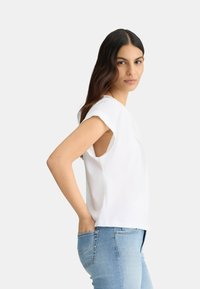 Haut blanc à manches courtes avec des détails découpés, associé à un jean ajusté bleu clair avec des coutures décoratives sur les poches arrière.