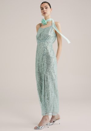 Sequined mint green dress with a fitted bodice, side slit, and loose back straps. Accompanied by a light mint scarf and silver heeled sandals.