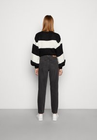 Svartvitt randig stickad tröja med lösa ärmar, kombinerad med grå raka jeans och vita sneakers. Utsikt bakifrån.